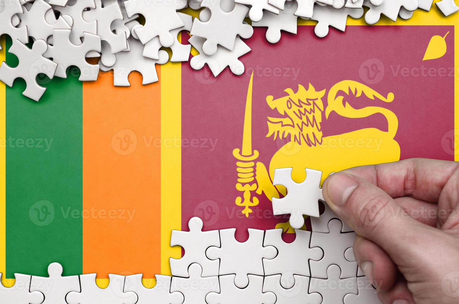 Sri Lanka flag is depicted on a table on which the human hand folds a puzzle of white color photo