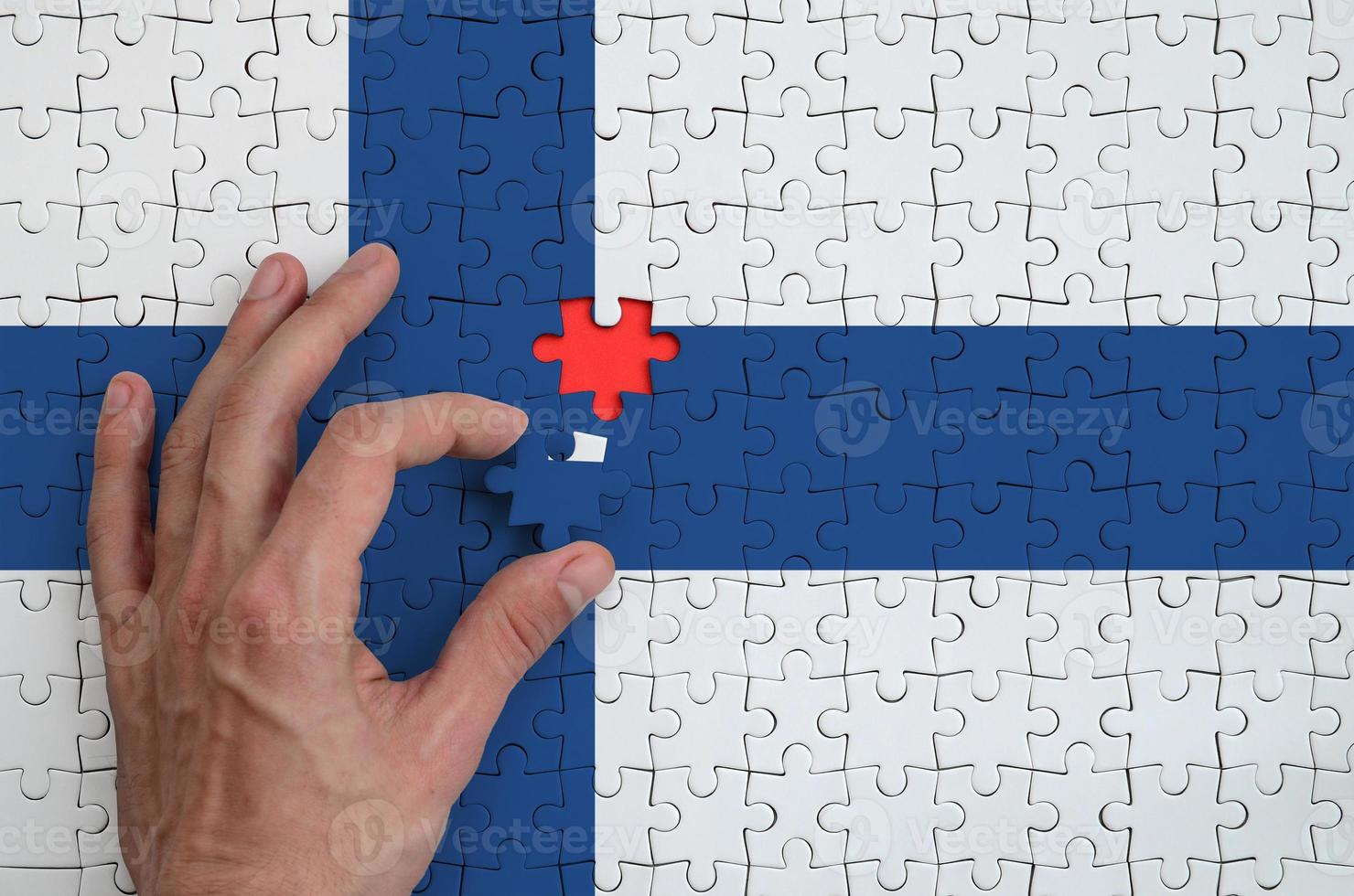 Finland flag is depicted on a puzzle, which the man's hand completes to fold photo