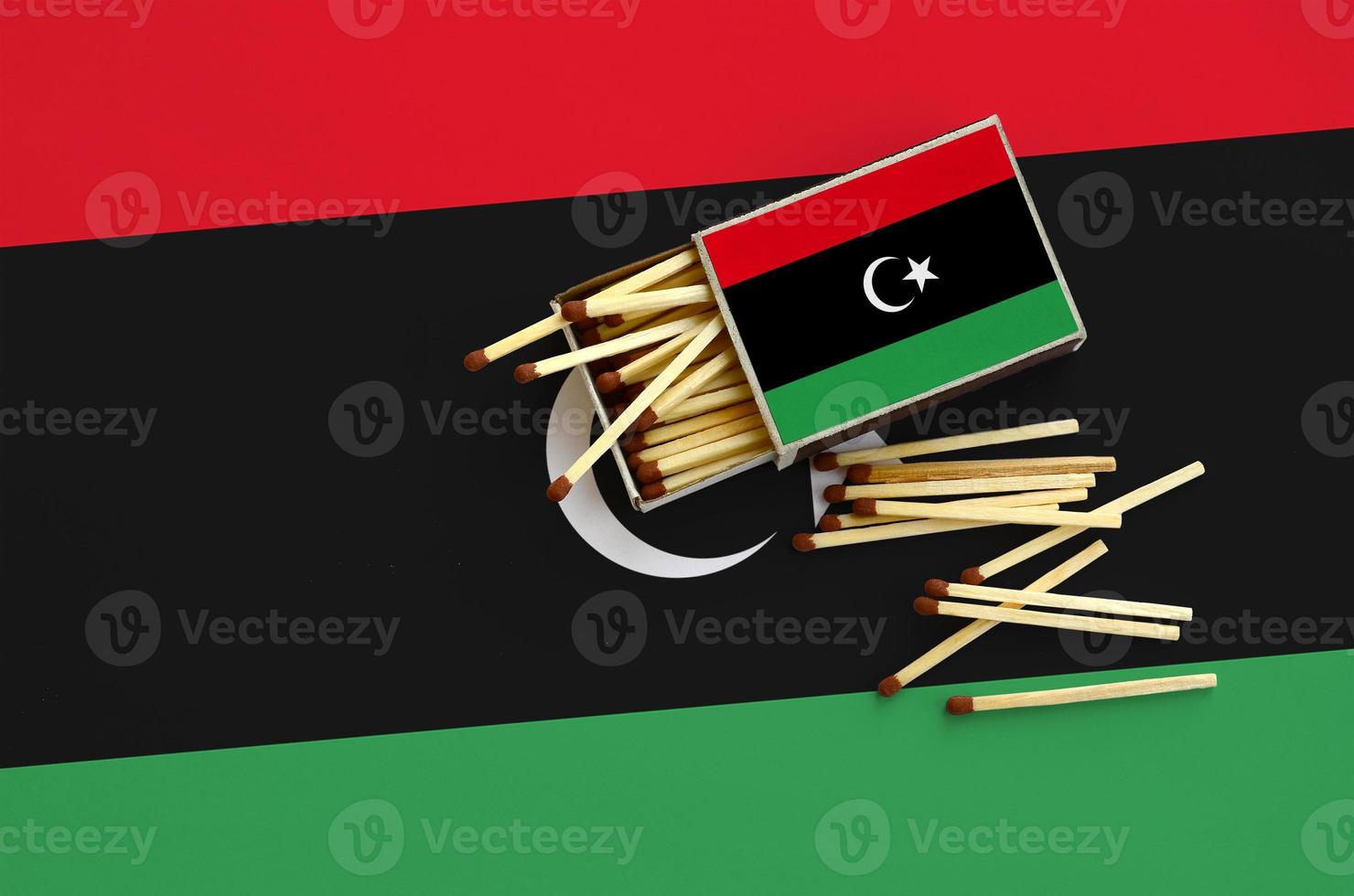 Libya flag is shown on an open matchbox, from which several matches fall and lies on a large flag photo