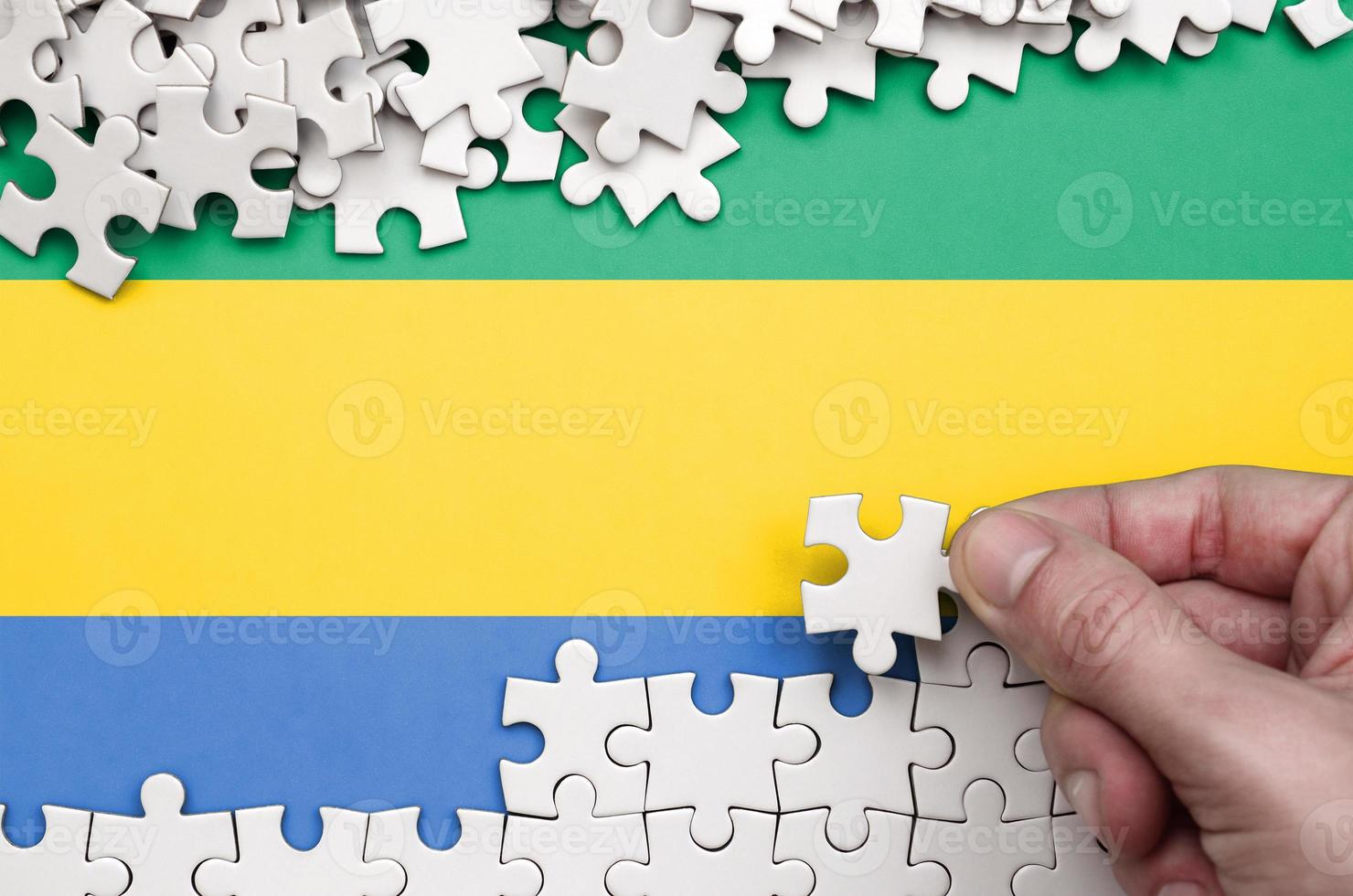 Gabon flag is depicted on a table on which the human hand folds a puzzle of white color photo