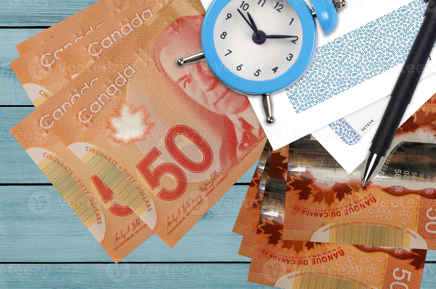50 Canadian dollars bills and alarm clock with pen and envelopes. Tax season concept, payment deadline for credit or loan. Financial operations using postal service photo