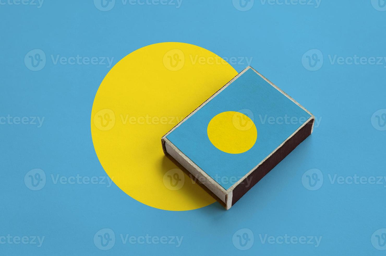 Palau flag is pictured on a matchbox that lies on a large flag photo