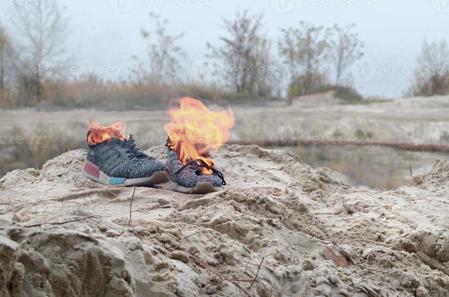 Burning sports sneakers or gym shoes on fire stand on sandy beach coast. Athlete burned out. Physical exertion during training concept photo