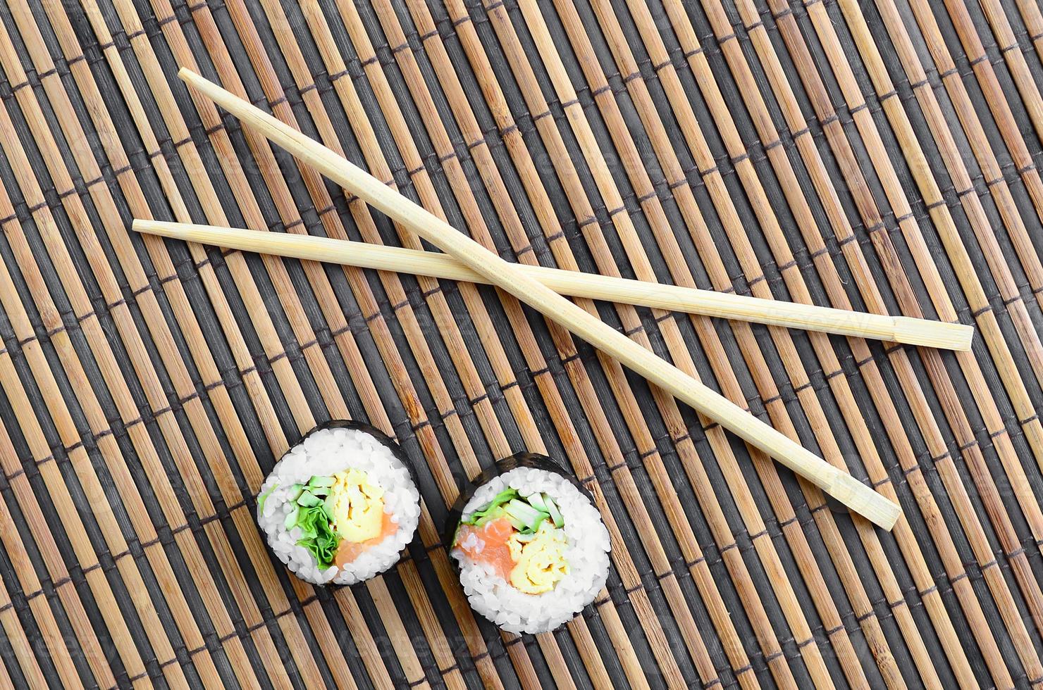 Sushi rolls and wooden chopsticks lie on a bamboo straw serwing mat. Traditional Asian food. Top view. Flat lay minimalism shot with copy space photo