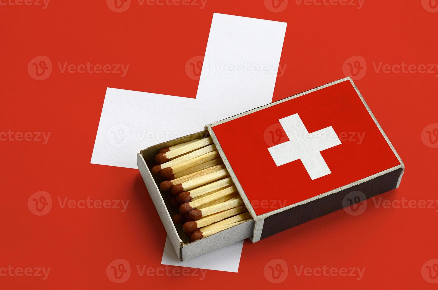 Switzerland flag is shown in an open matchbox, which is filled with matches and lies on a large flag photo