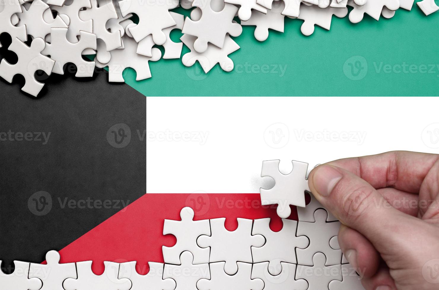 Kuwait flag is depicted on a table on which the human hand folds a puzzle of white color photo