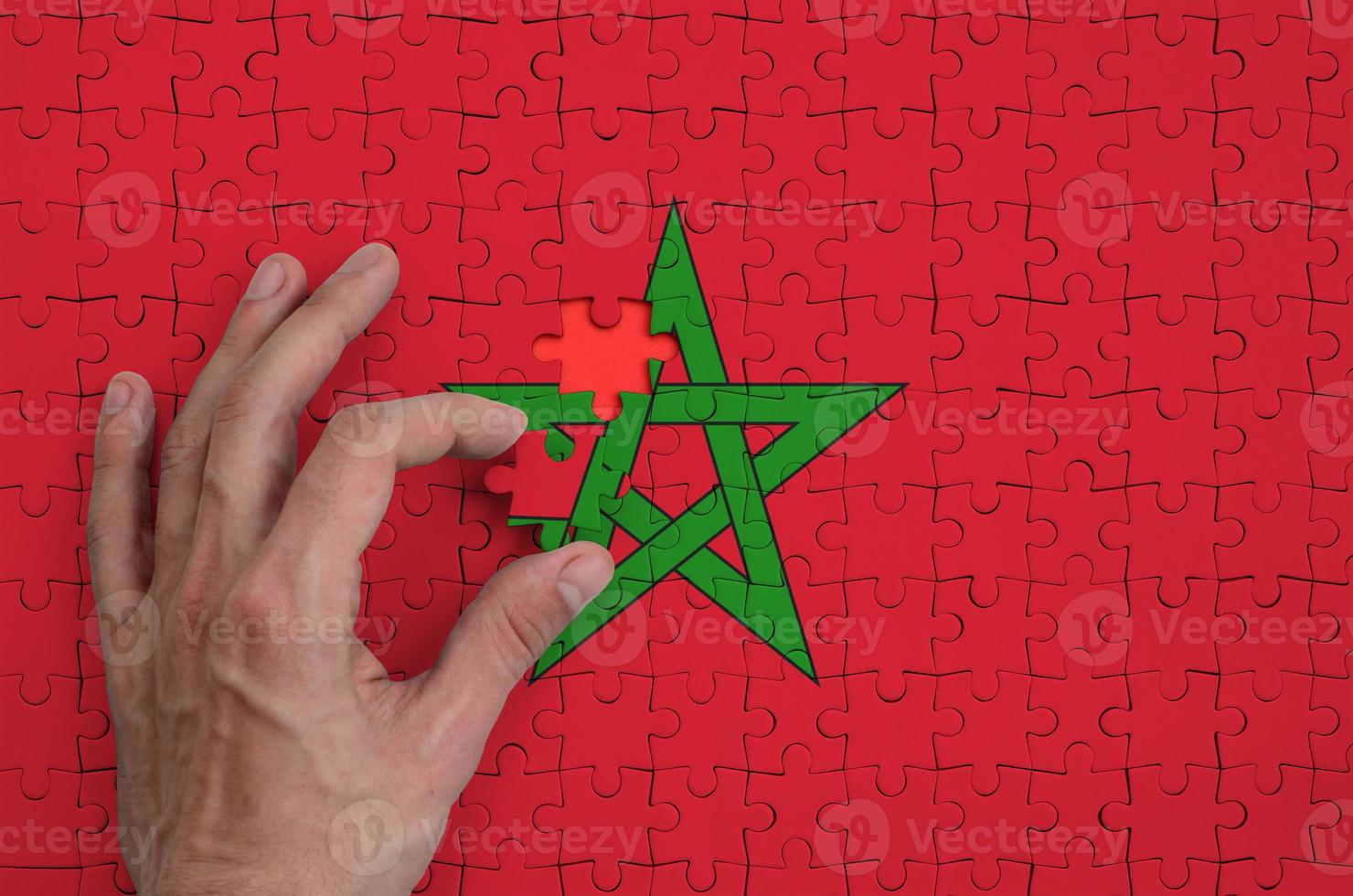 Morocco flag is depicted on a puzzle, which the man's hand completes to fold photo