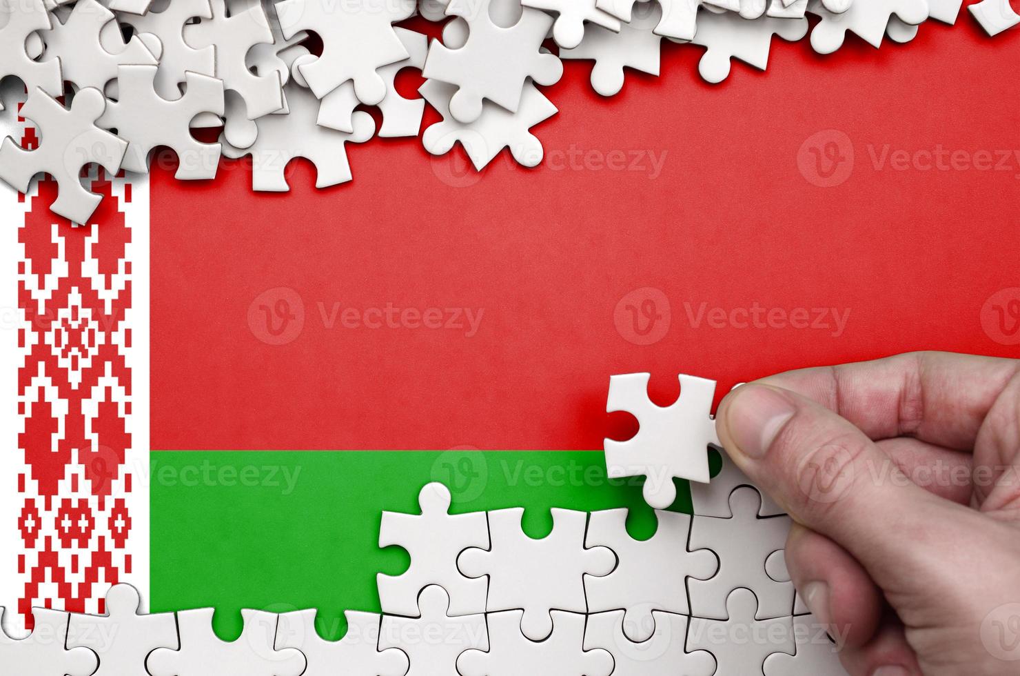 Belarus flag is depicted on a table on which the human hand folds a puzzle of white color photo