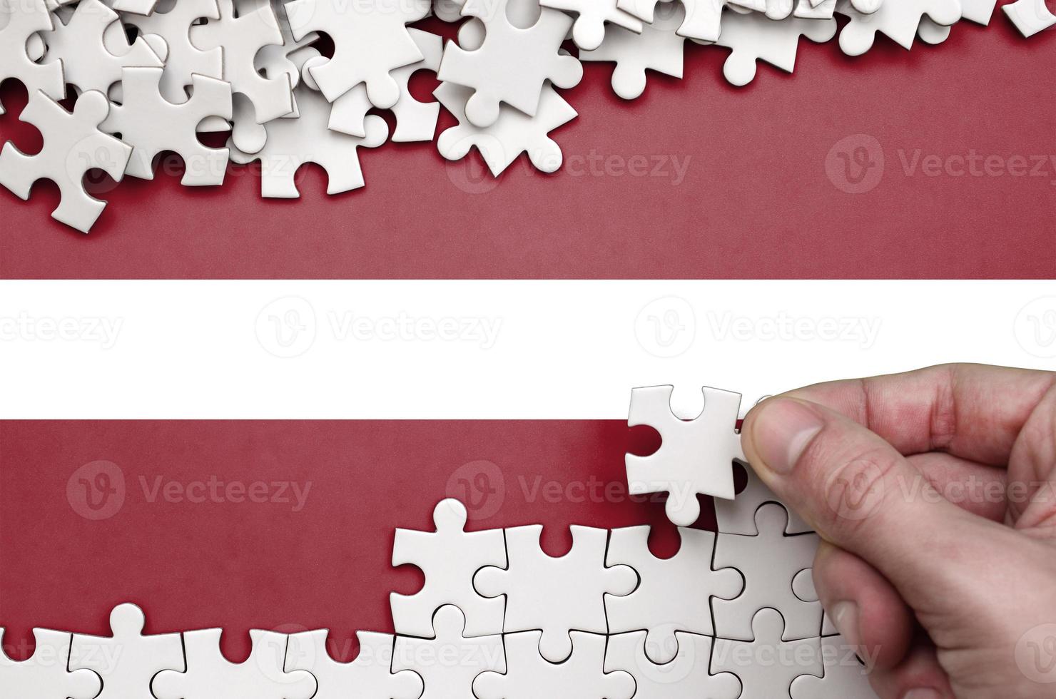 Latvia flag is depicted on a table on which the human hand folds a puzzle of white color photo