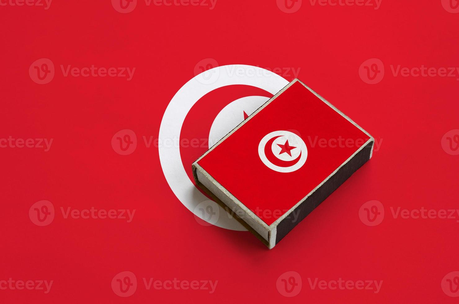 Tunisia flag is pictured on a matchbox that lies on a large flag photo