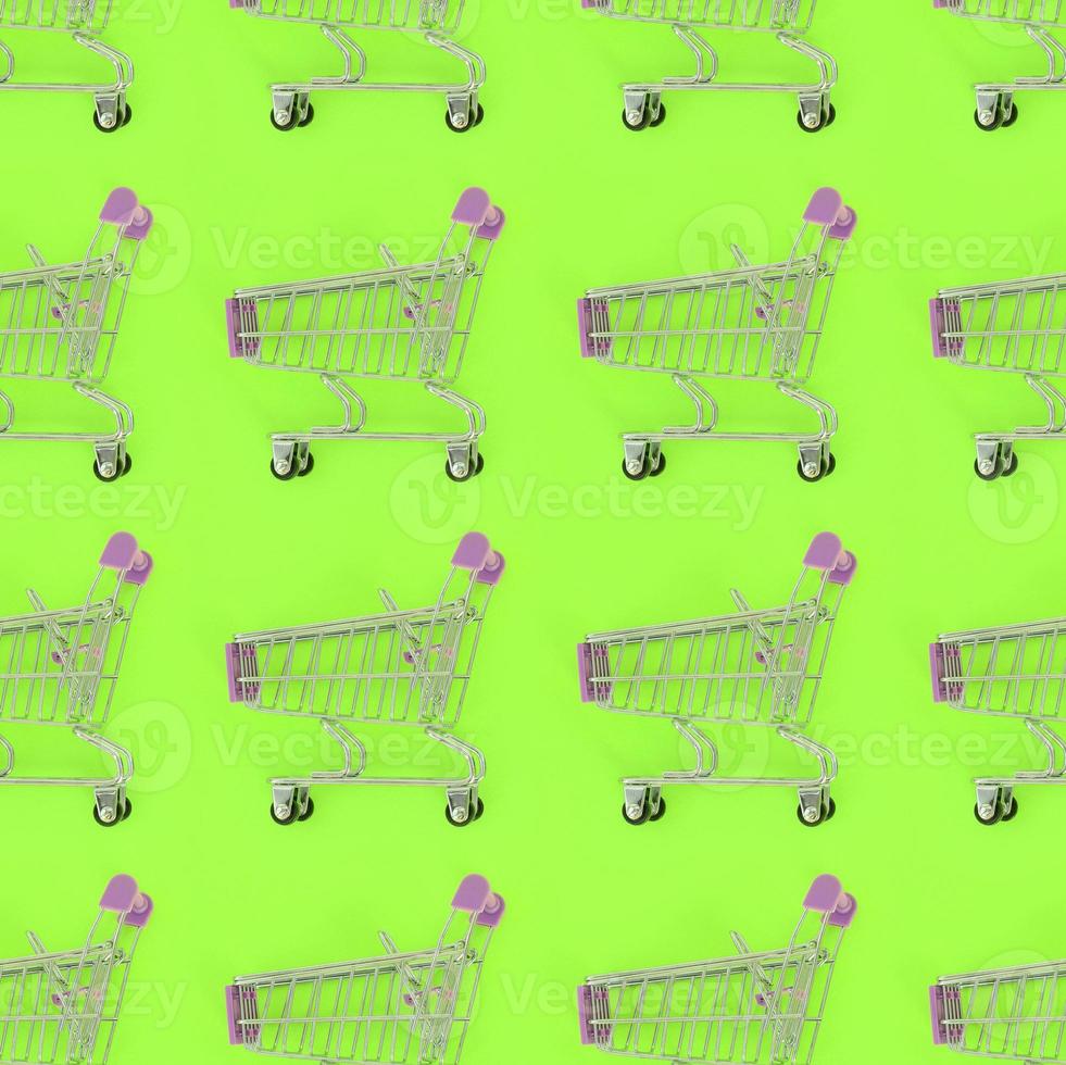 Shopping addiction, shopping lover or shopaholic concept. Many small empty shopping carts perform a pattern on a pastel colored paper background. Flat lay composition, top view photo