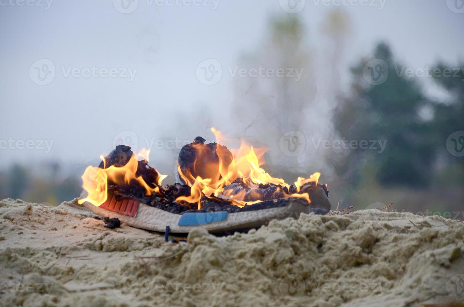 Burning sports sneakers or gym shoes on fire stand on sandy beach coast. Athlete burned out. Physical exertion during training concept photo