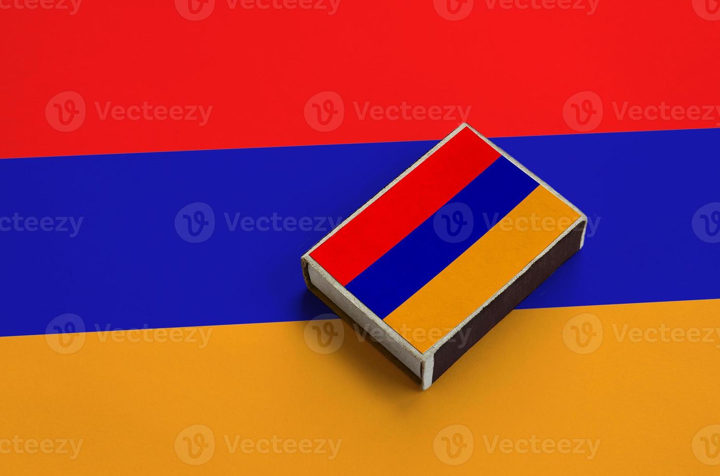 Armenia flag is pictured on a matchbox that lies on a large flag photo
