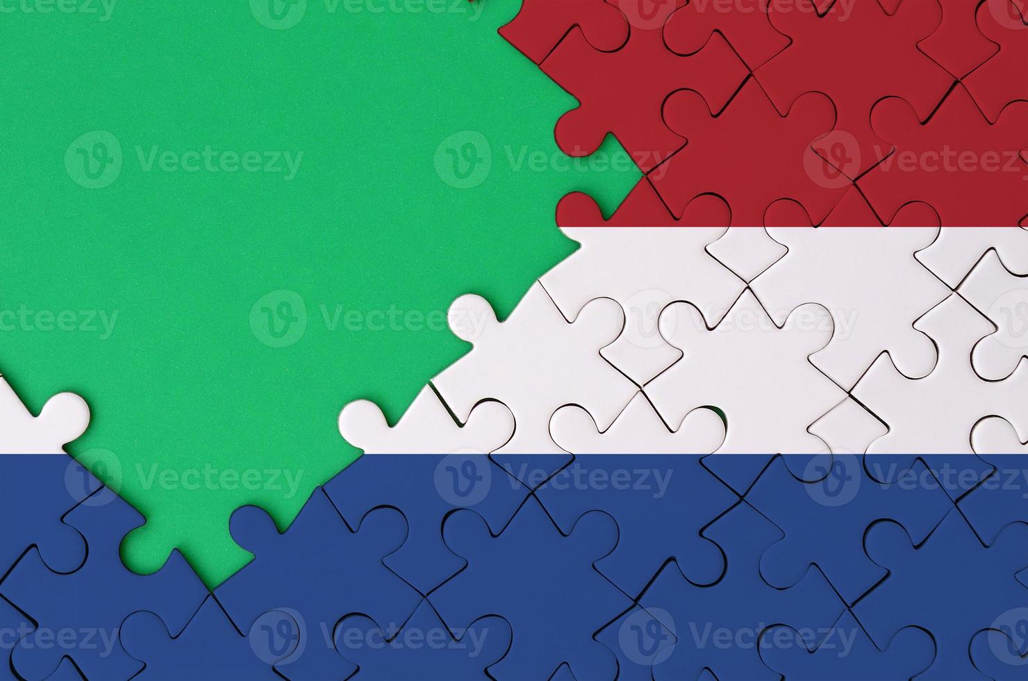 Netherlands flag is depicted on a completed jigsaw puzzle with free green copy space on the left side photo