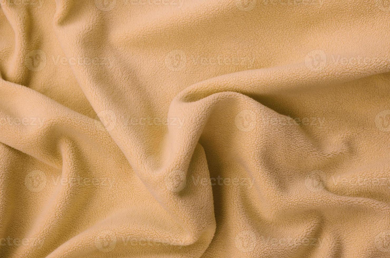The blanket of furry orange fleece fabric. A background of light orange soft plush fleece material with a lot of relief folds photo