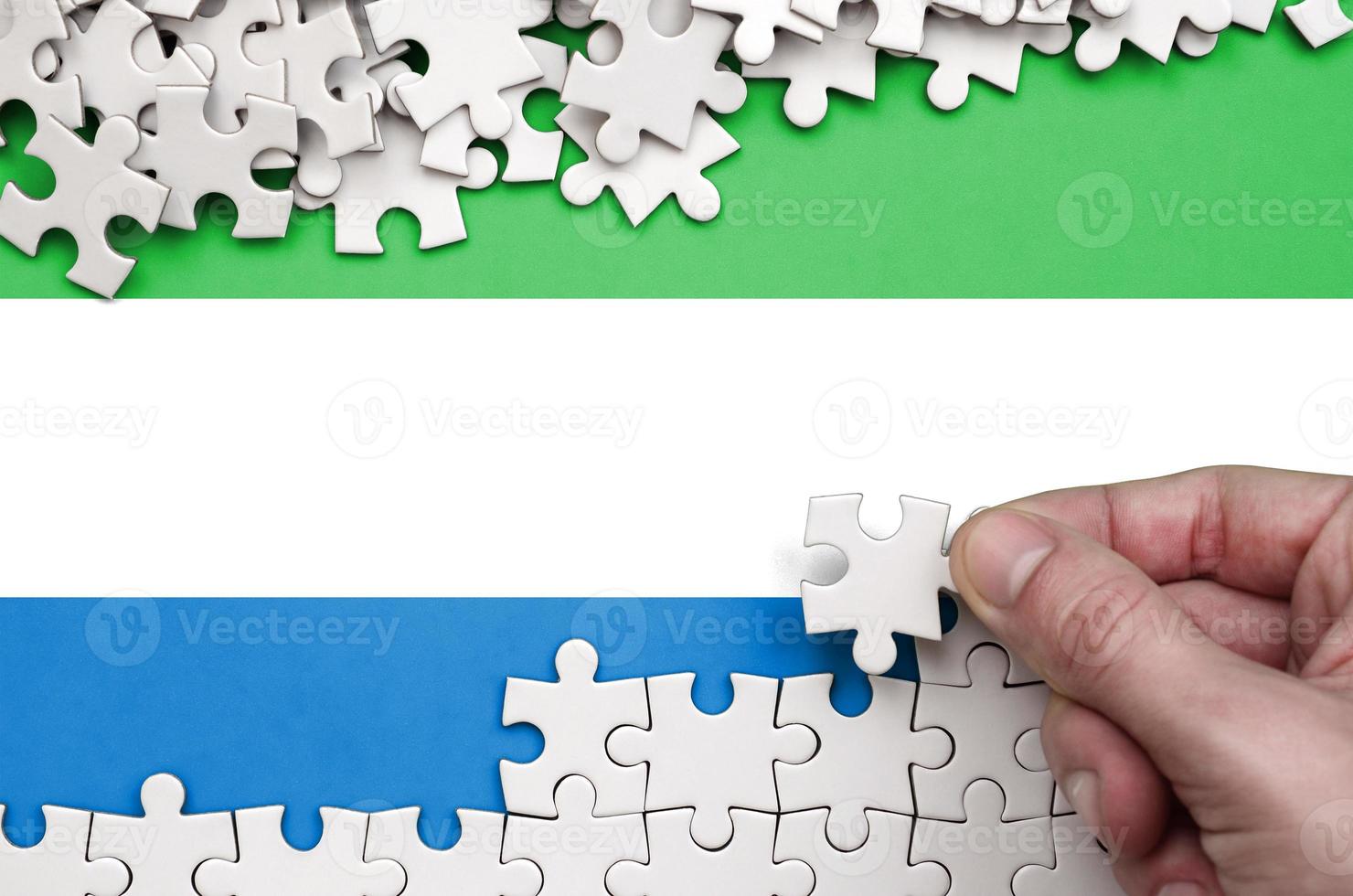 Sierra Leone flag is depicted on a table on which the human hand folds a puzzle of white color photo