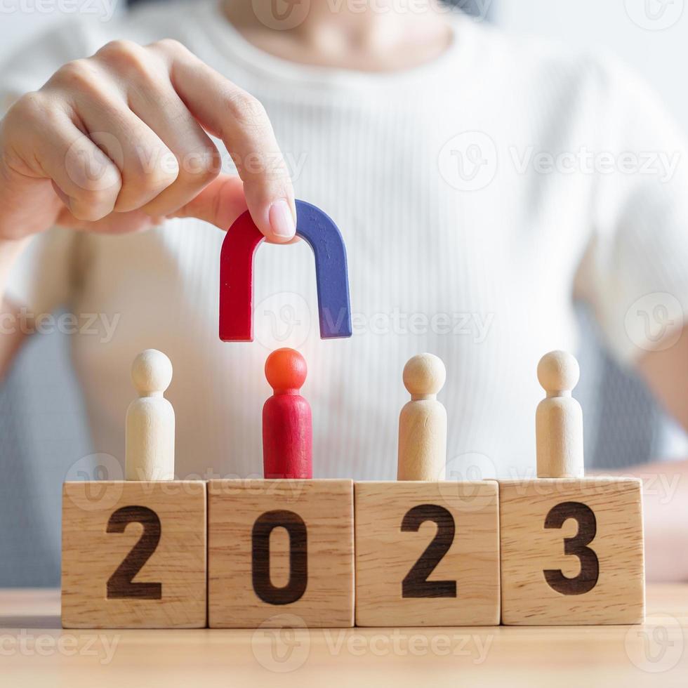 hand holding magnet and pulling man wooden figure from the crowd employee with 2023 Year block. Human resource management, Recruitment, Teamwork, strategy, toxic people and leadership Concepts photo