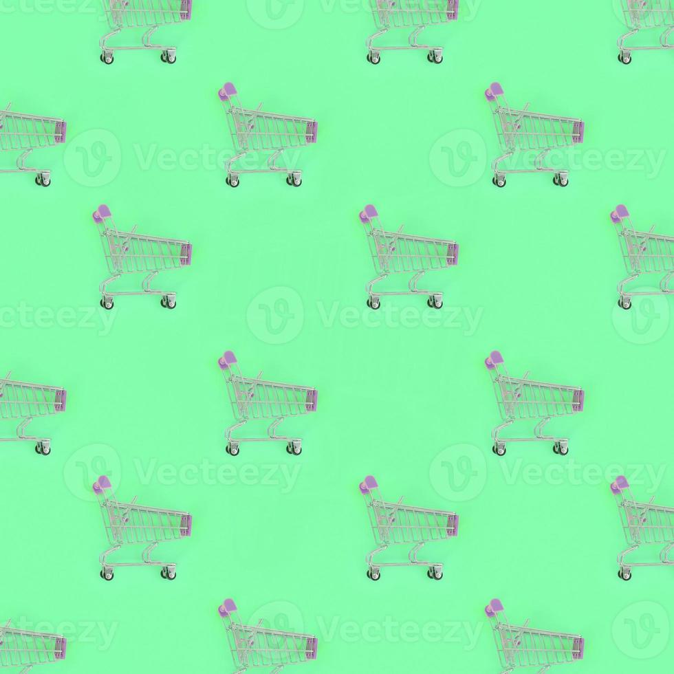 Shopping addiction, shopping lover or shopaholic concept. Many small empty shopping carts perform a pattern on a pastel colored paper background. Flat lay composition, top view photo