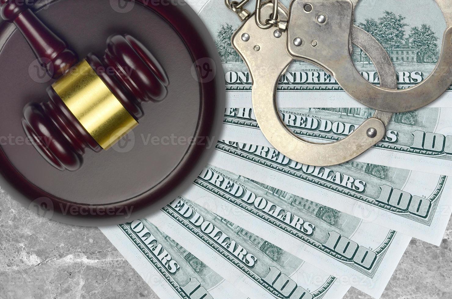 100 US dollars bills and judge hammer with police handcuffs on court desk. Concept of judicial trial or bribery. Tax avoidance photo