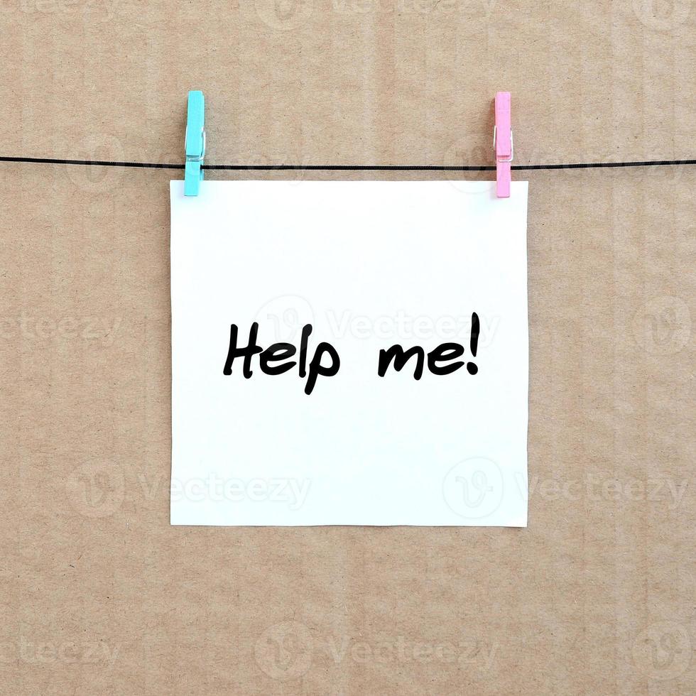 Help me Note is written on a white sticker that hangs with a clothespin on a rope on a background of brown cardboard photo