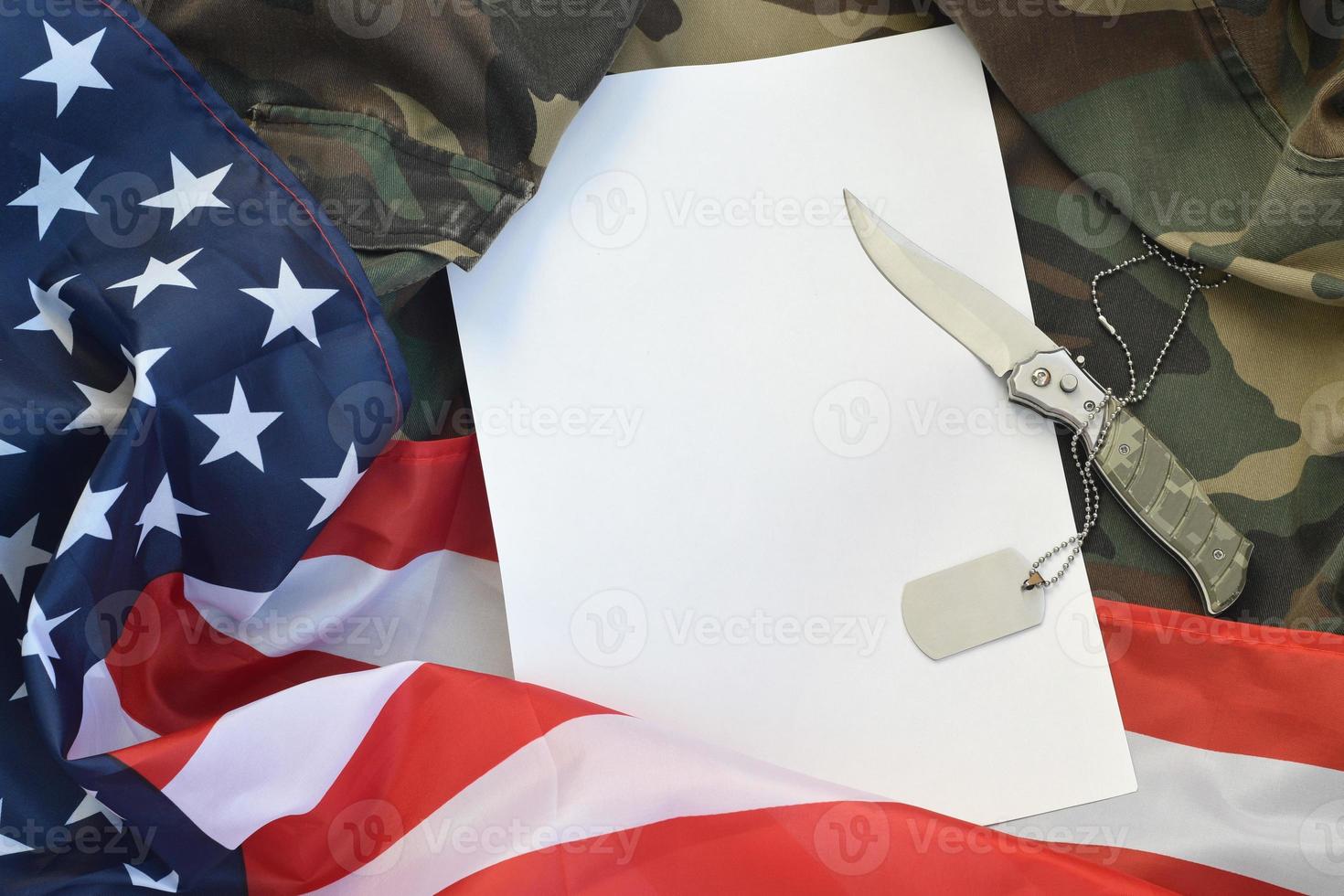 el papel en blanco se encuentra con un cuchillo y un collar de etiqueta de perro del ejército en uniforme de camuflaje y bandera estadounidense foto