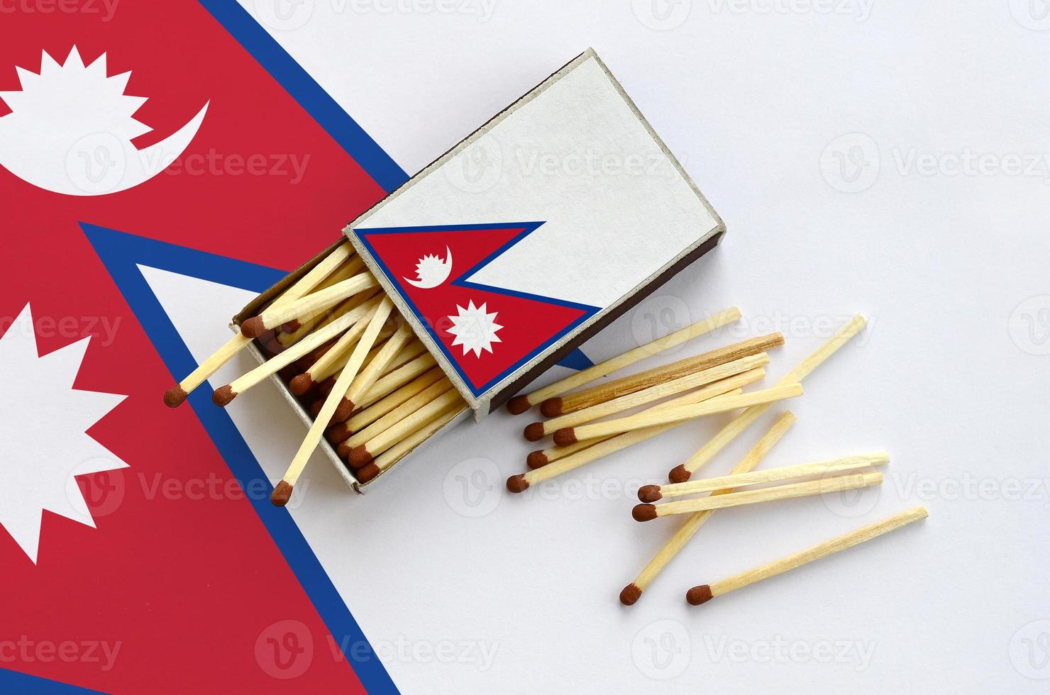 Nepal flag is shown on an open matchbox, from which several matches fall and lies on a large flag photo