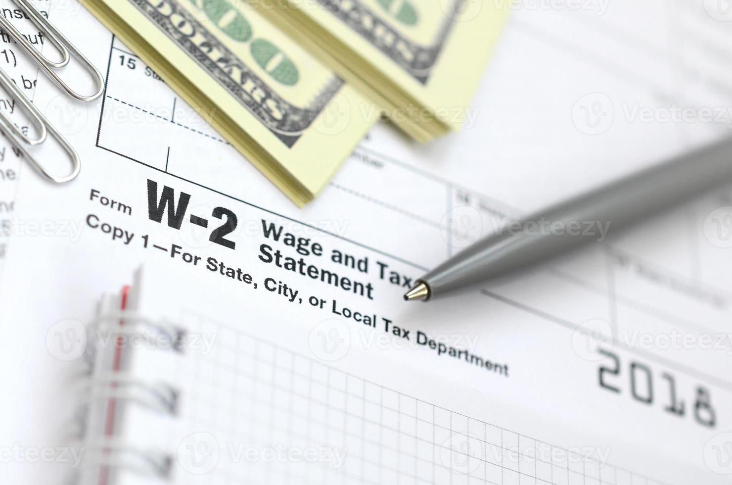 el bolígrafo, el cuaderno y los billetes de dólar se encuentran en el formulario de impuestos w-2 declaración de salarios e impuestos. la hora de pagar impuestos foto