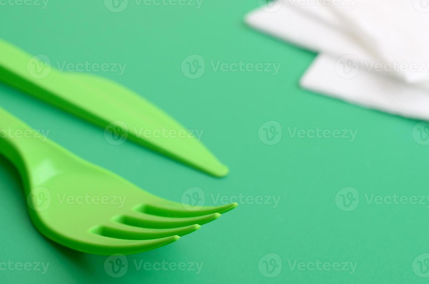 Disposable plastic cutlery green. Plastic fork and knife lie on a green background surface next to napkins photo