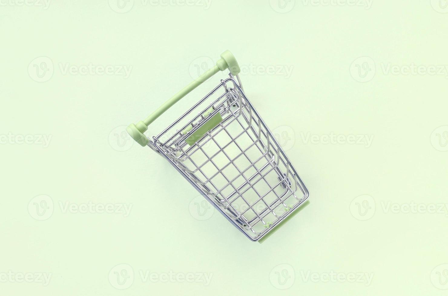 Small shopping cart lies on a lime background. Minimalism flat lay photo