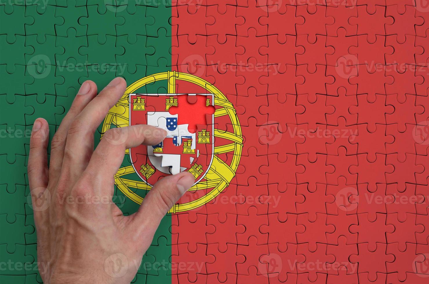 Portugal flag is depicted on a puzzle, which the man's hand completes to fold photo