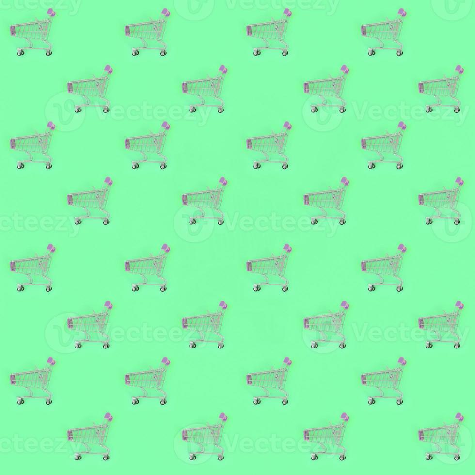 Shopping addiction, shopping lover or shopaholic concept. Many small empty shopping carts perform a pattern on a pastel colored paper background. Flat lay composition, top view photo