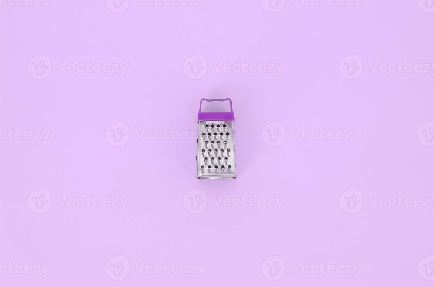 Stainless steel grater lies on a pastel colored paper. Kitchen accessories. Tools for cooking. Flat lay top view photo