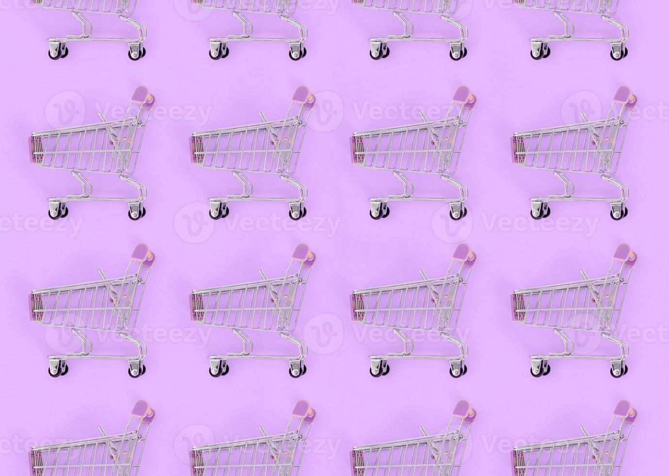 Shopping addiction, shopping lover or shopaholic concept. Many small empty shopping carts perform a pattern on a pastel colored paper background. Flat lay composition, top view photo