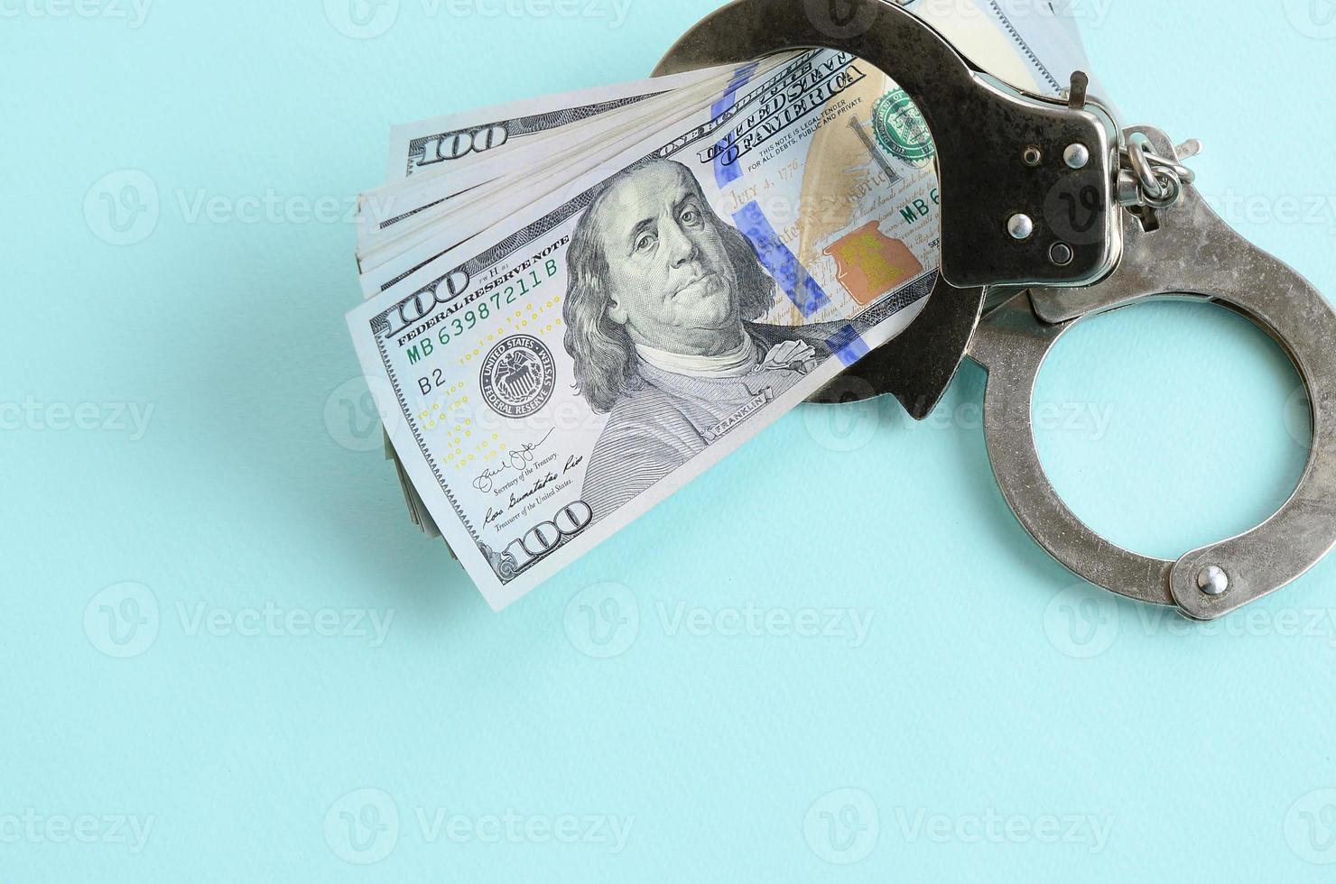Silver police handcuffs and hundred dollar bills lies on light blue background photo