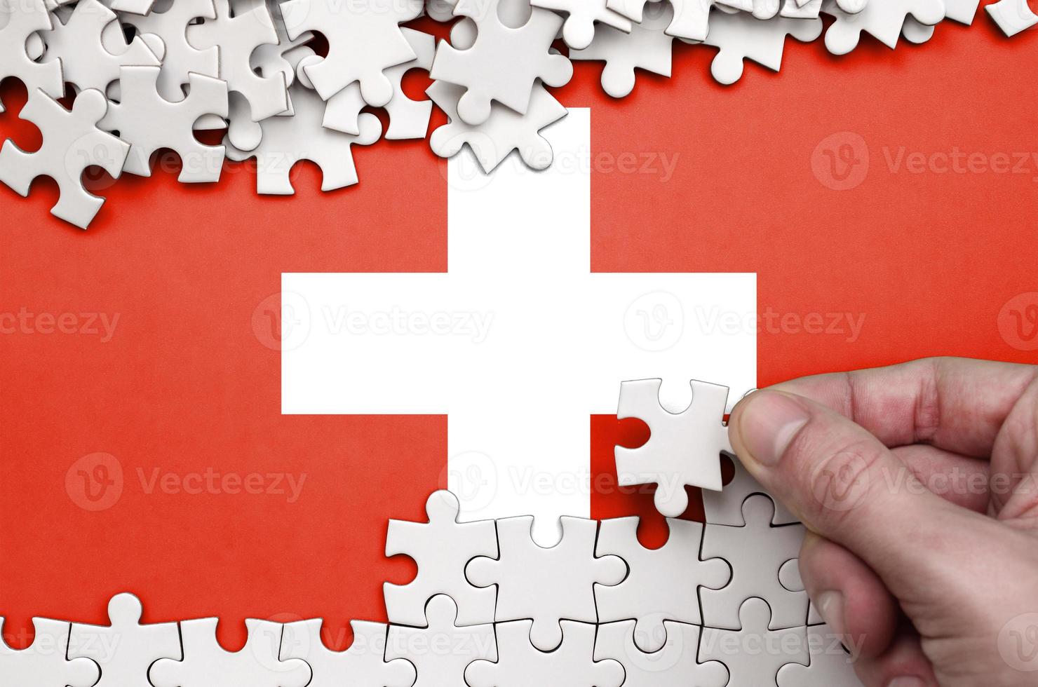 la bandera suiza está representada en una mesa en la que la mano humana dobla un rompecabezas de color blanco foto