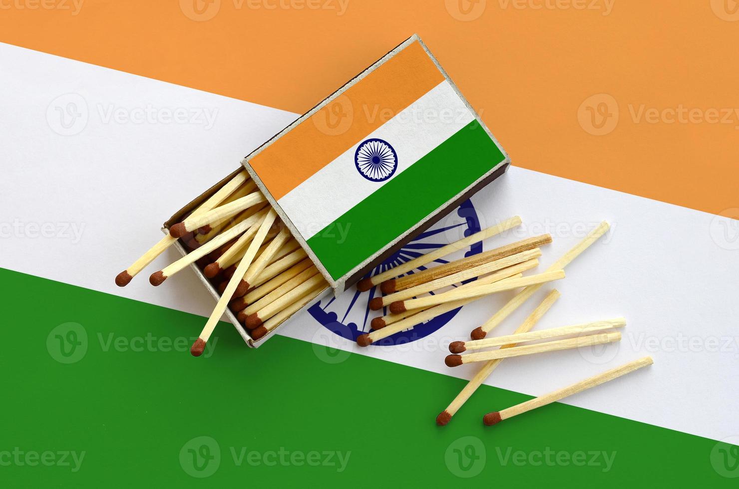 India flag is shown on an open matchbox, from which several matches fall and lies on a large flag photo
