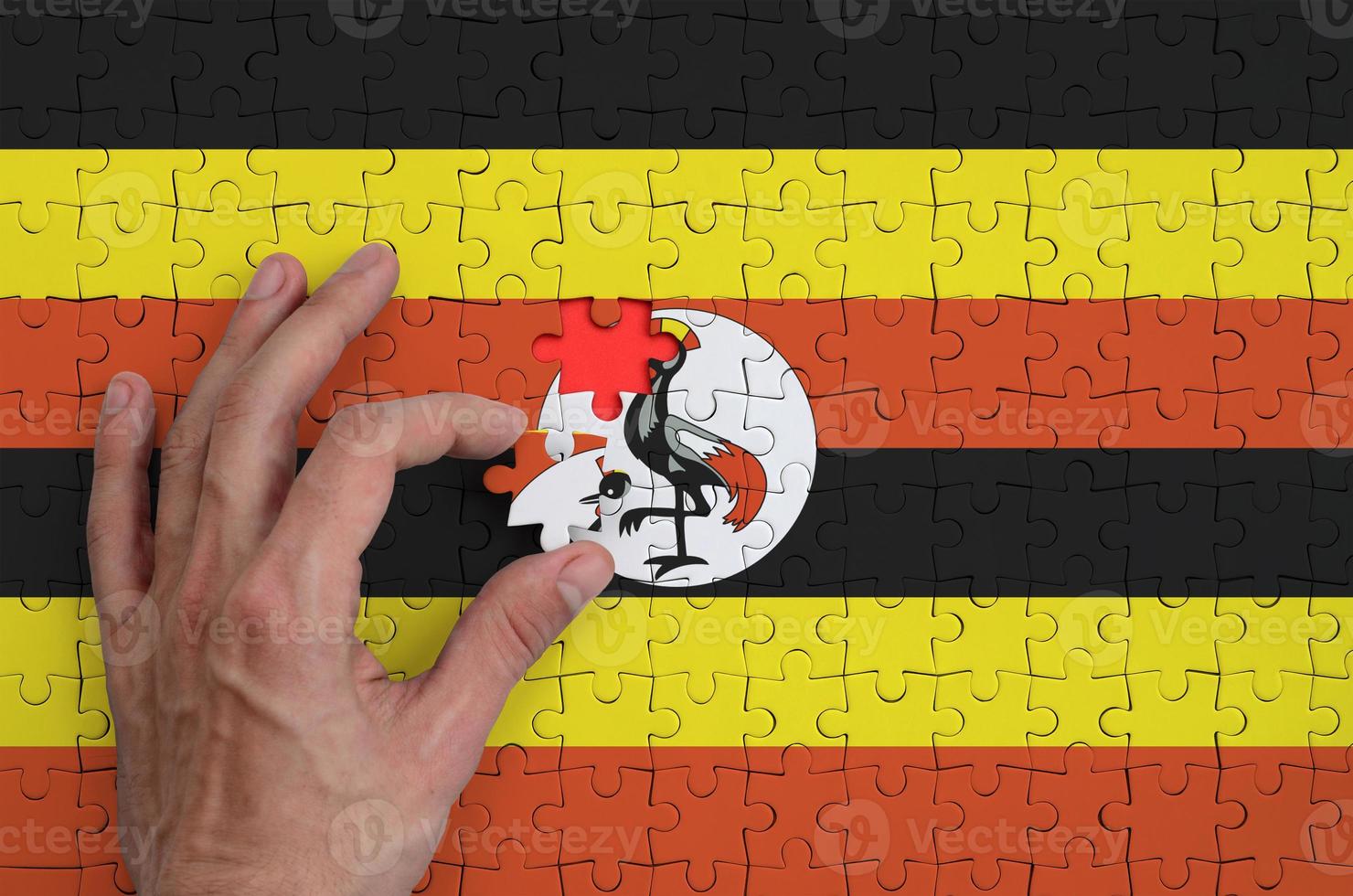 Uganda flag is depicted on a puzzle, which the man's hand completes to fold photo