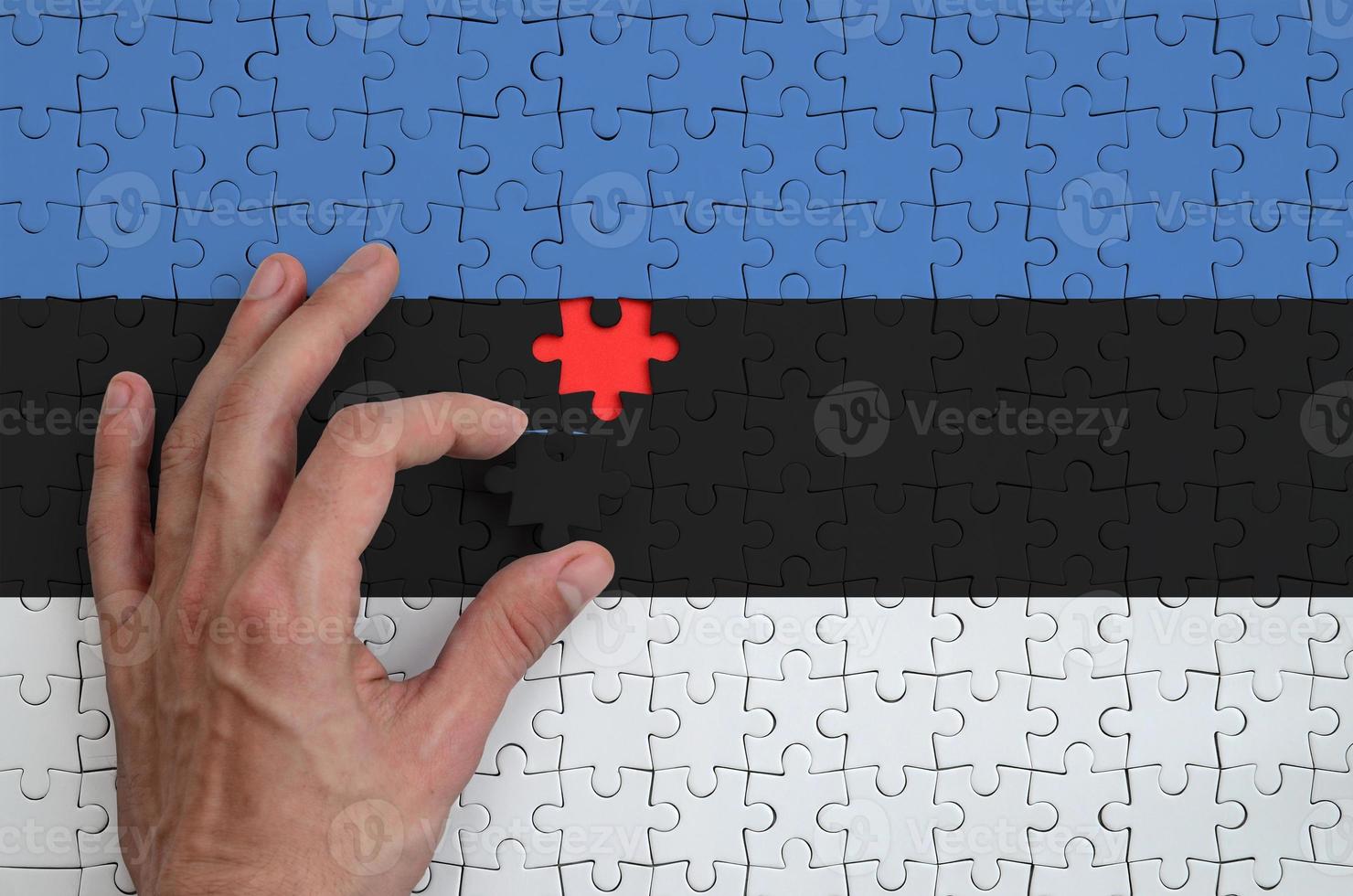 Estonia flag is depicted on a puzzle, which the man's hand completes to fold photo