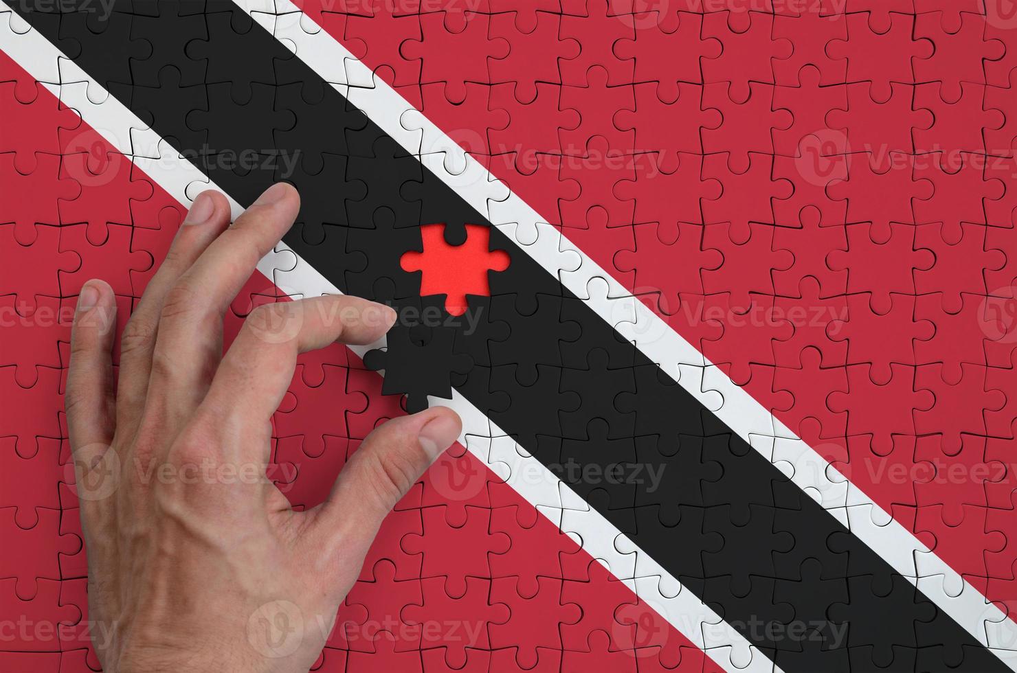 Trinidad and Tobago flag is depicted on a puzzle, which the man's hand completes to fold photo