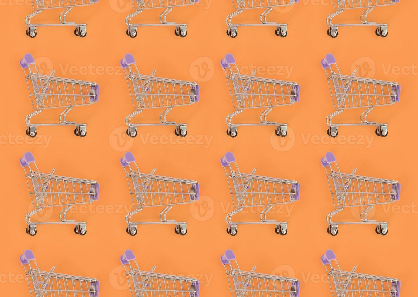 adicción a las compras, amante de las compras o concepto de adicto a las compras. muchos pequeños carros de compras vacíos realizan un patrón sobre un fondo de papel de color pastel. composición plana, vista superior foto