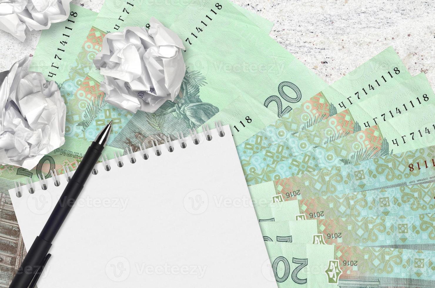 20 Ukrainian hryvnias bills and balls of crumpled paper with blank notepad. Bad ideas or less of inspiration concept. Searching ideas for investment photo