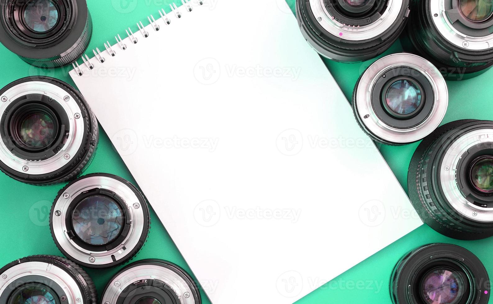 Several photographic lenses and white notebook lie on a bright turquoise background. Copy space photo