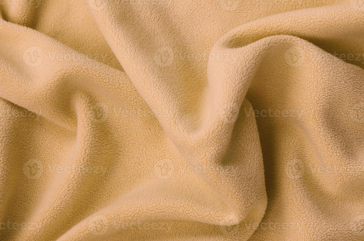 The blanket of furry orange fleece fabric. A background of light orange soft plush fleece material with a lot of relief folds photo