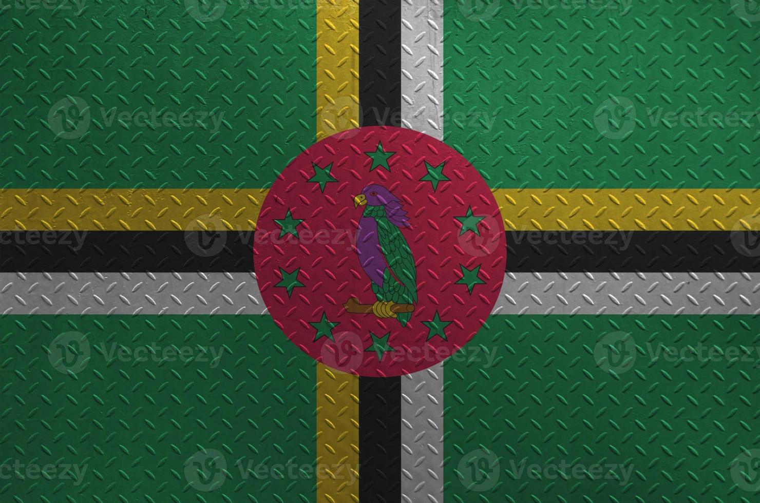 Dominica flag depicted in paint colors on old brushed metal plate or wall closeup. Textured banner on rough background photo