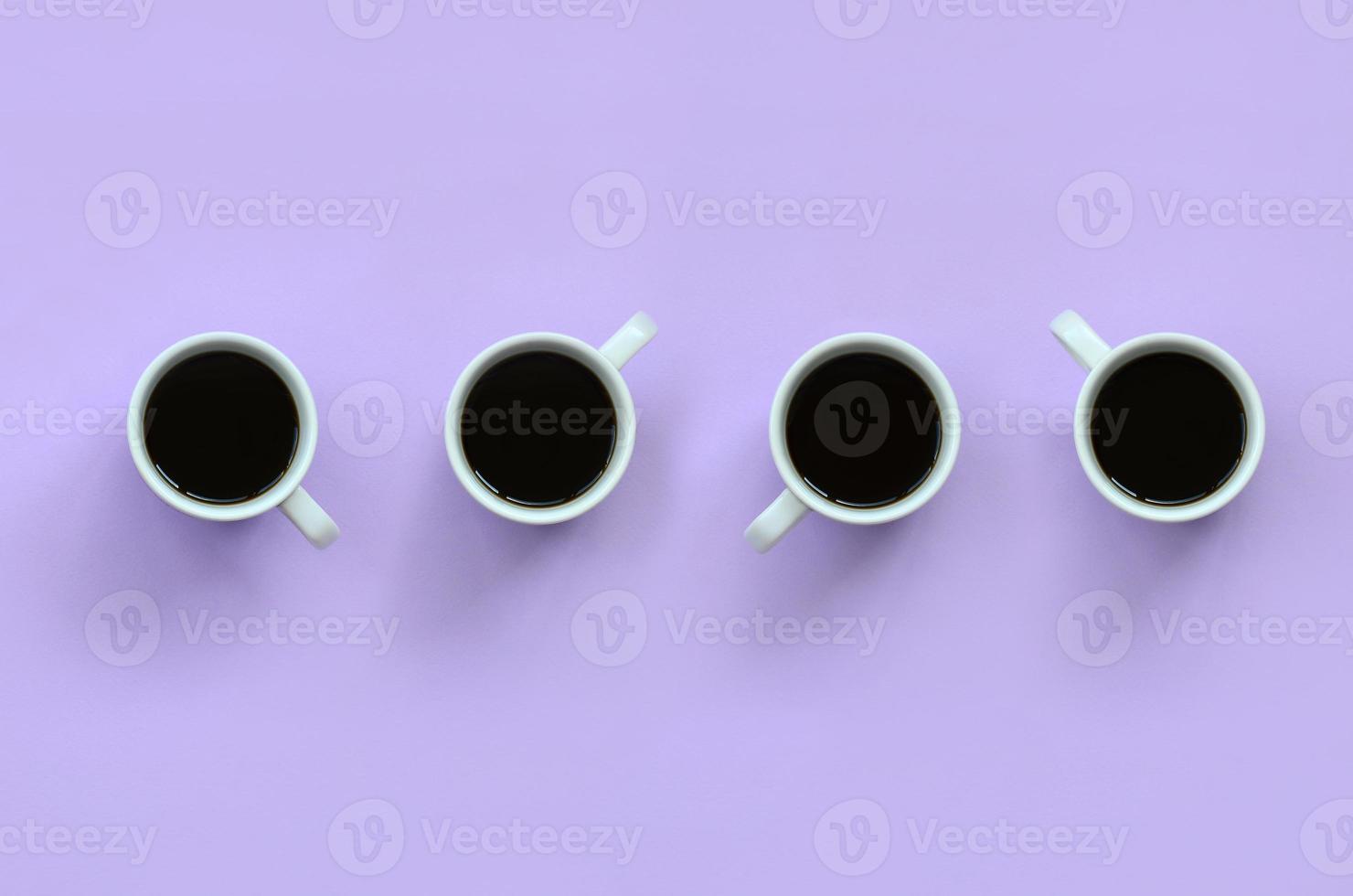 muchas tazas pequeñas de café blanco sobre fondo de textura de papel de color violeta pastel de moda en concepto mínimo foto