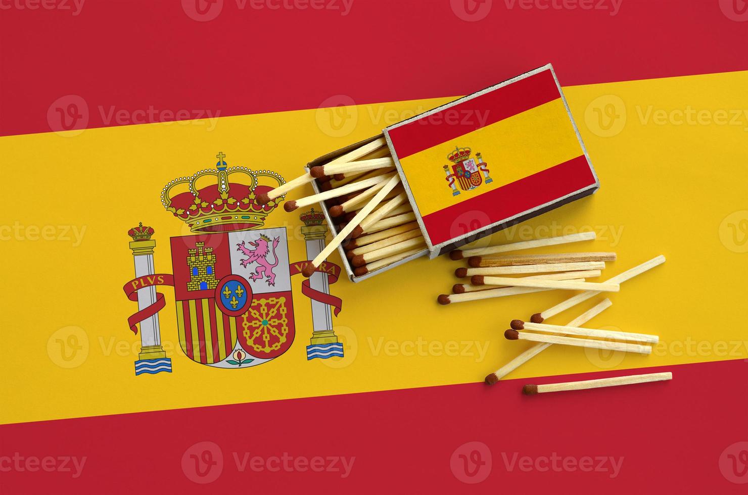 Spain flag is shown on an open matchbox, from which several matches fall and lies on a large flag photo