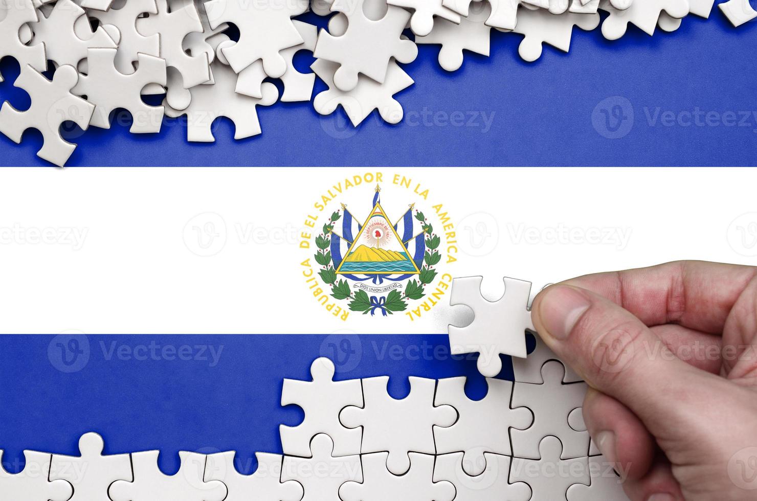 El Salvador flag is depicted on a table on which the human hand folds a puzzle of white color photo