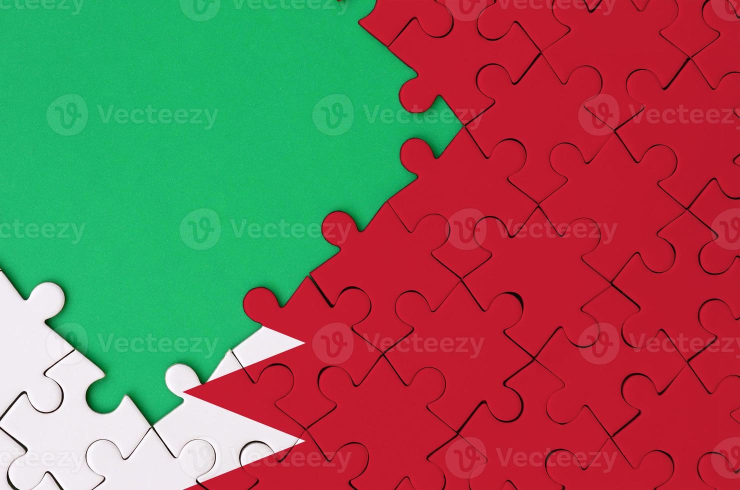 Bahrain flag is depicted on a completed jigsaw puzzle with free green copy space on the left side photo