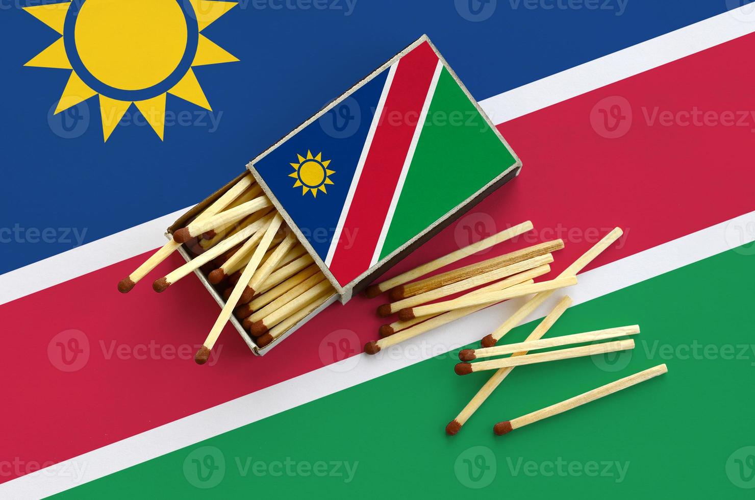 Namibia flag is shown on an open matchbox, from which several matches fall and lies on a large flag photo