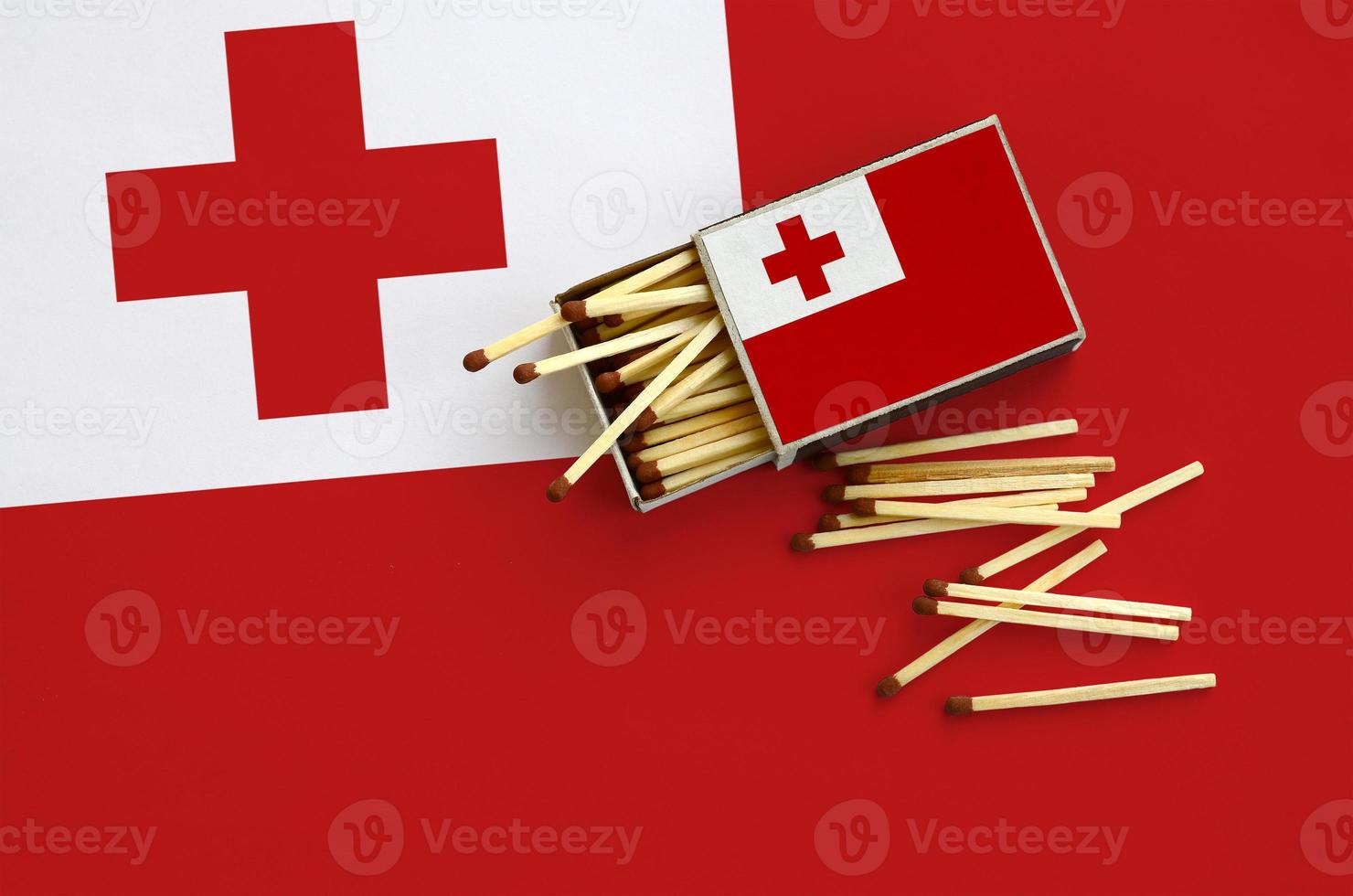 Tonga flag is shown on an open matchbox, from which several matches fall and lies on a large flag photo